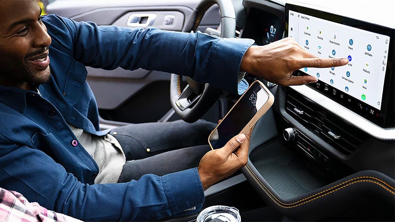 Man holding phone in front of infotainment screen of 2027 Ford Explorer